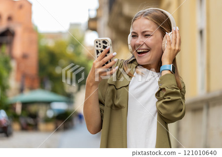 Happy woman in wireless headphones dancing, listening favorite energetic music singing on street 121010640