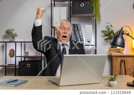 Senior happy Caucasian businessman working on laptop shocked by sudden victory at home office desk 121010649