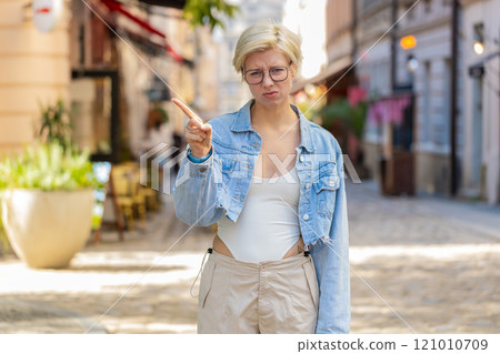 Upset young blonde woman reacting to unpleasant awful idea shaking finger at camera on city street Upset young blonde woman reacting to unpleasant awful idea shaking finger at camera on city street 121010709