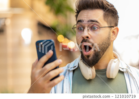 Upset young man using smartphone typing browsing, loses becoming shocked bad news on city street 121010719