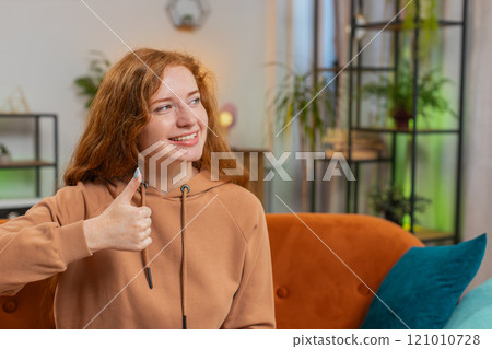 Portrait of smiling Caucasian young woman showing double thumbs up sitting on sofa couch at home Portrait of smiling Caucasian young woman showing double thumbs up sitting on sofa couch at home 121010728
