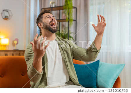 Sad young man feeling loneliness, nervous breakdown, crying shouting on sofa in living room at home Sad young man feeling loneliness, nervous breakdown, crying shouting on sofa in living room at home 121010733