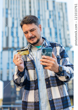 Frustrated mature businessman using credit card and mobile phone standing on downtown city street 121010761