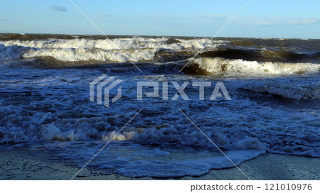 Stormy sea with dark waves crashing against the shore under a cloudy sky during late afternoon Stormy sea with dark waves crashing against the shore under a cloudy sky during late afternoon 121010976