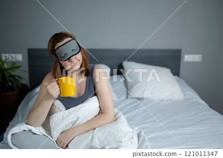 A Woman is Happily Enjoying Her Morning Coffee While Sitting in a Cozy Bedroom Setting 121011347