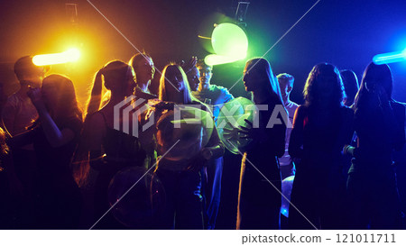 Young cheerful girls and boys, friends attending party, celebrating birthday or holiday together,. cheerfully dancing under neon lights 121011711