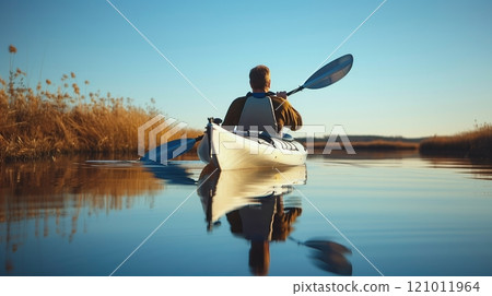 A man enjoys a peaceful kayak ride on a tranquil lake, promoting serenity, mindfulness, and fitness. A man enjoys a peaceful kayak ride on a tranquil lake, promoting serenity, mindfulness, and fitness. 121011964