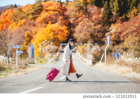 Women's trip: A woman walking with a carry bag along a road with beautiful autumn leaves 121012011