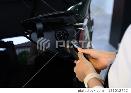 Hands connecting a charging cable to an electric car. Transportation and clean energy initiatives concept 121012732
