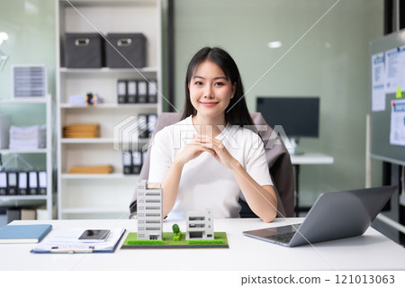 Young real estate agent worker working with laptop and tablet at table in office and small house beside it. Young real estate agent worker working with laptop and tablet at table in office and small house beside it. 121013063