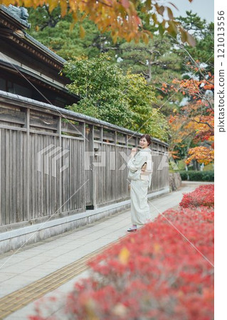 A woman in a kimono walking next to an old house 121013556