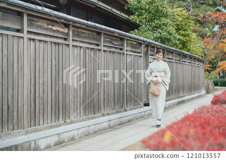 A woman in a kimono walking next to an old house 121013557
