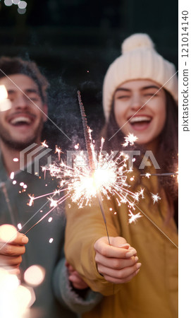 Group of young adults celebrating New Year with sparklers outdoors, joyful winter scene Group of young adults celebrating New Year with sparklers outdoors, joyful winter scene 121014140