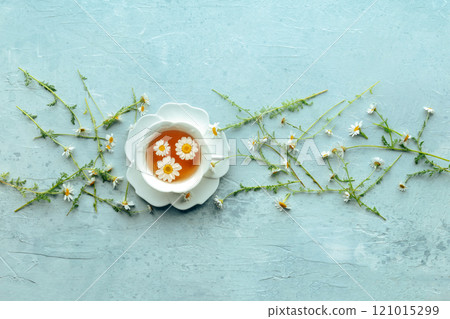 Chamomile flower tea. A tea cup with infusing blossoms, overhead flat lay 121015299