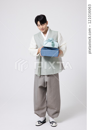 Portrait of a young man wearing hanbok and holding a luxurious holiday gift 121016063