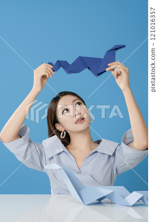 Portrait of a woman sitting and posing while holding a blue snake folded out of paper 121016357