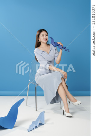 A woman sitting and posing in front of a blue snake folded out of paper 121016375