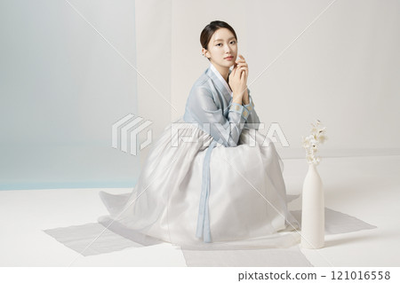 A beautiful woman wearing a luxurious and elegant hanbok sitting next to a vase 121016558