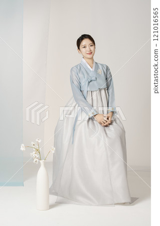 A beautiful woman wearing a luxurious and elegant hanbok sitting next to a vase 121016565