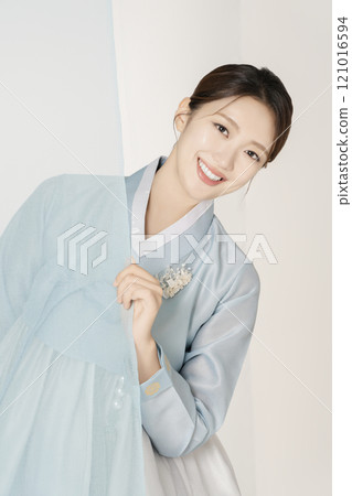 A beautiful woman wearing a luxurious and elegant Hanbok, standing behind a blue cloth 121016594