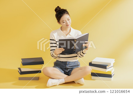 A college student wearing casual clothes and sitting on the floor reading 121016654