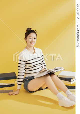 A college student wearing casual clothes and sitting on the floor reading 121016656
