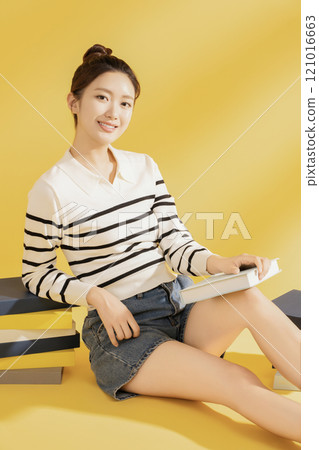 A college student wearing casual clothes and sitting on the floor reading 121016663