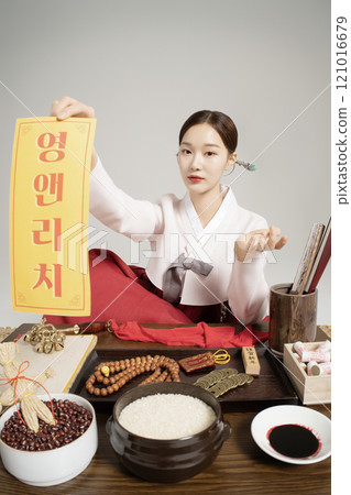 A shaman sitting wearing a hanbok and holding an amulet 121016679