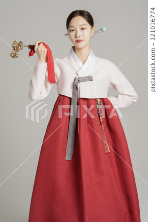 A woman in her 20s wearing a hanbok, wearing a colorful hairpin, and posing while holding a shaman bell. 121016774