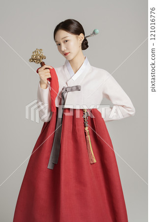 A woman in her 20s wearing a hanbok, wearing a colorful hairpin, and posing while holding a shaman bell. A woman in her 20s wearing a hanbok, wearing a colorful hairpin, and posing while holding a shaman bell. 121016776