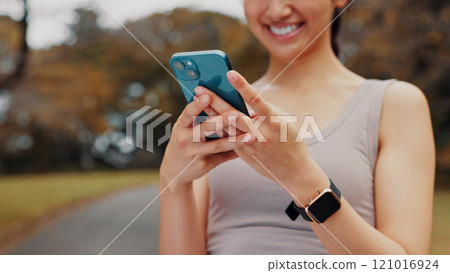 Smile, woman and hands with phone for fitness outdoor, communication and research of exercise application. Happy, athlete and mobile for gym membership, training schedule and workout routine in Japan 121016924