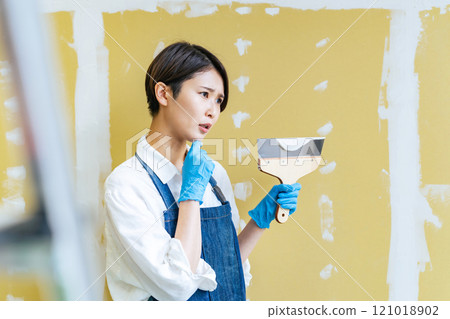 A woman thinking while applying putty to a plasterboard A woman thinking while applying putty to a plasterboard 121018902