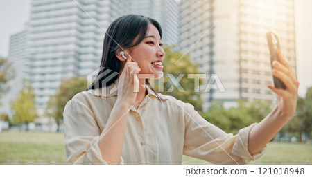 Happy, asian woman and video call with earphones in city for communication, conversation or chat. Japan, female person or talking with mobile smartphone for virtual discussion or app in an urban town Happy, asian woman and video call with earphones in city for communication, conversation or chat. Japan, female person or talking with mobile smartphone for virtual discussion or app in an urban town 121018948