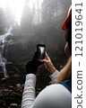 Capturing the Unmatched Beauty of Nature A Hiker with a Smartphone by a Waterfall 121019641