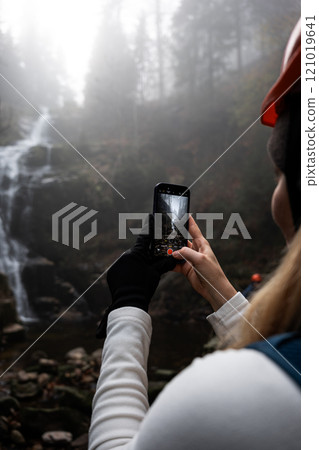 Capturing the Unmatched Beauty of Nature A Hiker with a Smartphone by a Waterfall 121019641