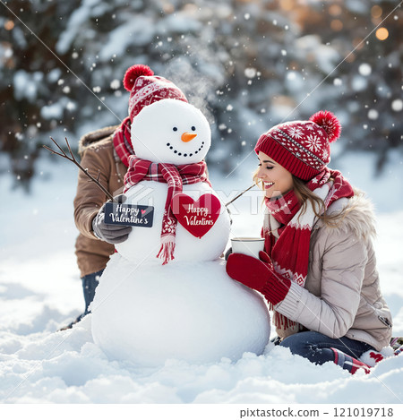 A cheerful snowman decorated with Valentine's hearts, with a woman enjoying a snowy winter day beside it 121019718