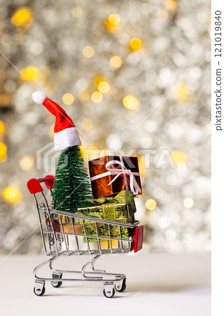 Vertical image of shopping trolley with gifts and christmas fairy lights with copy space background 121019840