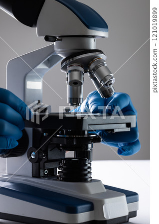 Vertical image hands of scientist in gloves using microscope and copy space on grey background 121019899