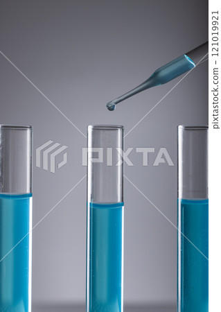 Vertical image of laboratory test tubes with blue liquid, pipette and copy space on grey background Vertical image of laboratory test tubes with blue liquid, pipette and copy space on grey background 121019921