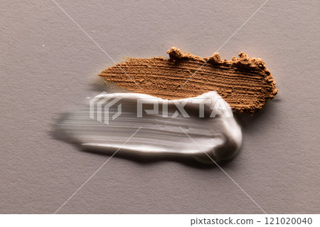 Close up of beauty product white and brown cream smudges with copy space on brown background Close up of beauty product white and brown cream smudges with copy space on brown background 121020040