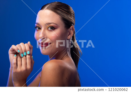 Portrait of caucasian woman wearing blue nail polish on blue background, copy space 121020062
