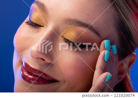 Caucasian woman with brown hair wearing golden eye shadow and blue nail polish on blue background Caucasian woman with brown hair wearing golden eye shadow and blue nail polish on blue background 121020074