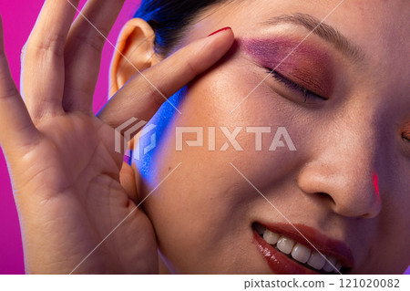 Asian woman with black hair wearing purple eye shadow and red nail polish on purple background 121020082