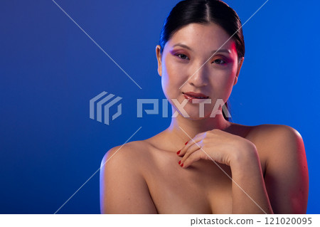 Portrait of asian woman wearing purple eye shadow and red nail polish on blue background, copy space 121020095