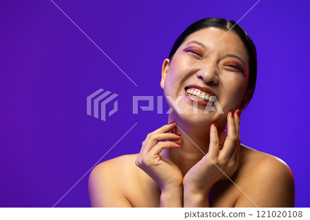 Asian woman wearing purple eye shadow and red nail polish on blue background, copy space 121020108