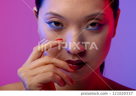 Portrait of asian woman wearing blue eyeliner and red nail polish on purple background 121020337