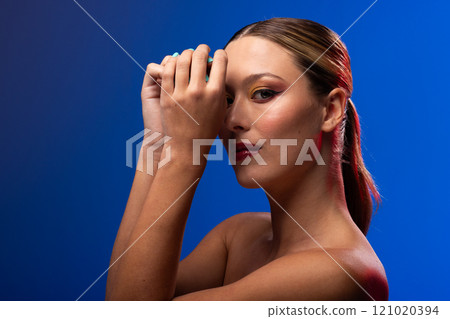 Portrait of caucasian woman wearing golden eye shadow and blue nail polish on blue background Portrait of caucasian woman wearing golden eye shadow and blue nail polish on blue background 121020394