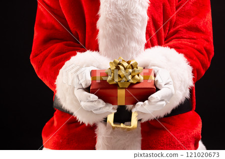 Santa claus holding red christmas present with copy space on black background 121020673