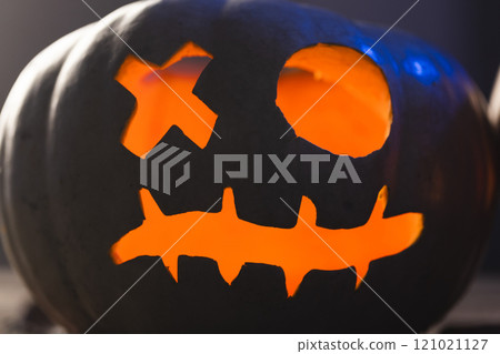 Carved pumpkin face illuminating with orange light on black background 121021127