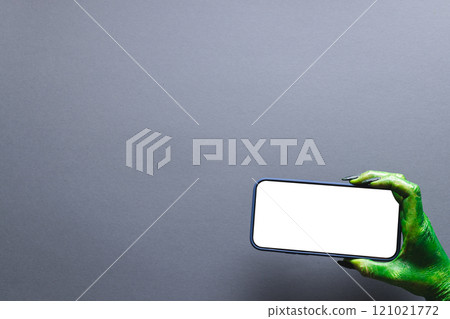 Green monster hand holding smartphone with copy space on grey background 121021772